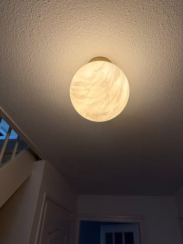 Klant toont de gemonteerde Carrara plafonnière die een mooi, warm licht aan het plafond geeft.