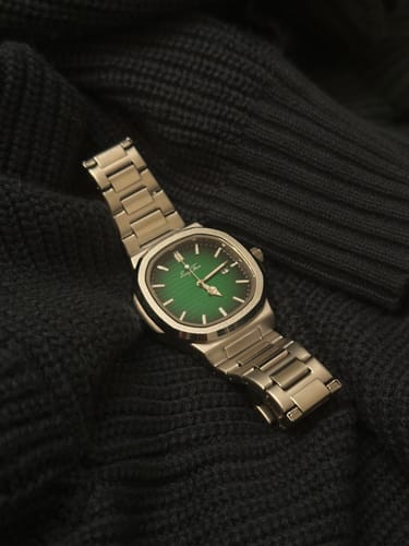 Reviewer's Lucky Fours Caspian watch with a green dial and silver band, resting on a dark, knitted fabric.