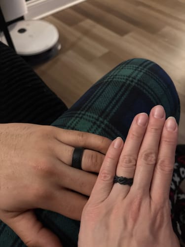 A couple's hands showing their black Couple Bundle Silicone Wedding Rings, featuring a wide band and a braided design.
