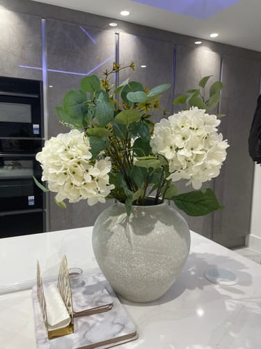 Customer's Arina Vase in Stone, styled with a bouquet of white flowers and greenery on a kitchen island.