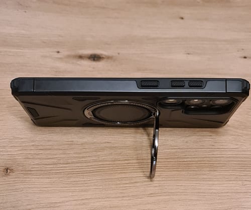 Kunde zeigt die schwarze Ultra-Robust Handyhülle, die mit dem ausgeklappten Ring waagerecht auf einem Tisch steht.