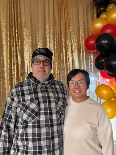 A customer couple posing happily together in front of a festive gold backdrop with balloons.