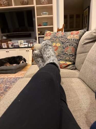 Reviewer relaxing on a sofa wearing cuffed, speckled Gripper Slipper Booties.