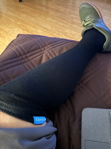 Reviewer's leg propped on a pillow, wearing a long, black Performance Eucalyptus Compression Sock.