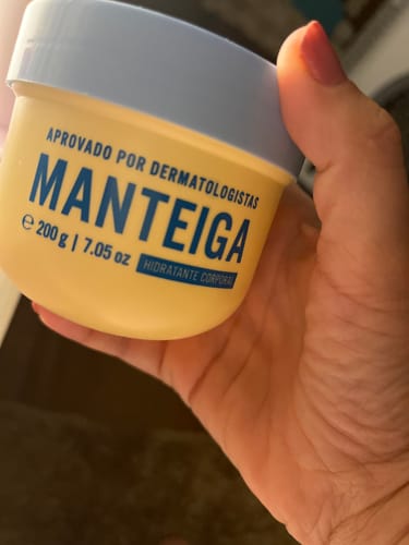 Cliente segurando o pote amarelo da Manteiga Hidratante na mão.