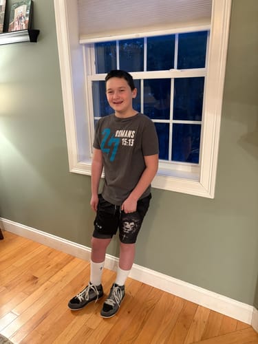 A customer wearing the black 'Lion' Youth Performance Shorts with a lion graphic while standing indoors.