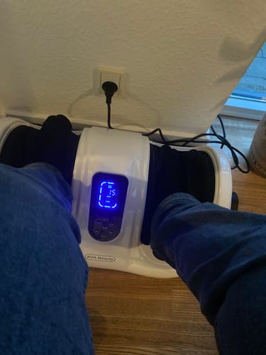 Anmelder med fødderne i det hvide fod- og lægmassageapparat. Det blå display viser 15, hvilket indikerer den resterende tid.