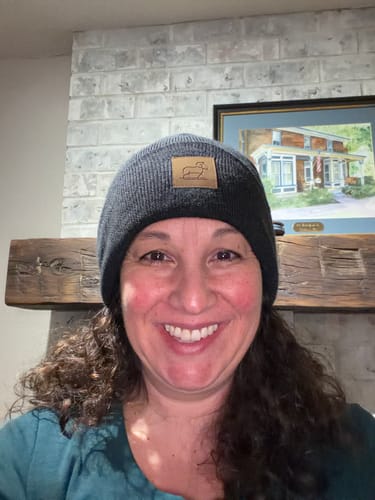 A smiling reviewer wearing the ribbed Carbon Black Baylor Beanie indoors.