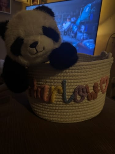Customer's personalized knitted basket with 'Marlowe' in multicolor yarn and a heart icon, holding a stuffed panda.