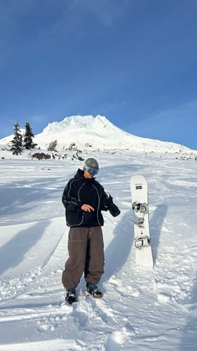 Customer wearing the black retro track snow jacket on a snowy mountain with their snowboard.