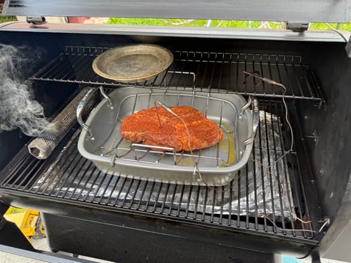Customer's seasoned chuck roast in a pan, placed inside a smoker before cooking.