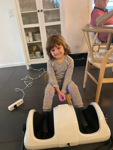 Anmelders barn sidder med fødderne i det hvide fod- og lægmassageapparat.