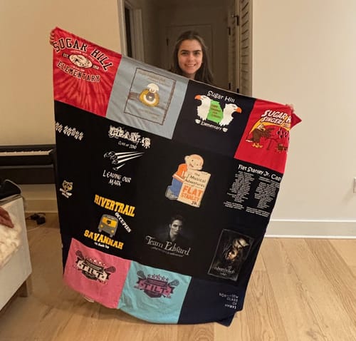 A customer holding up their large T-Shirt Quilt made from a colorful collage of t-shirt panels.