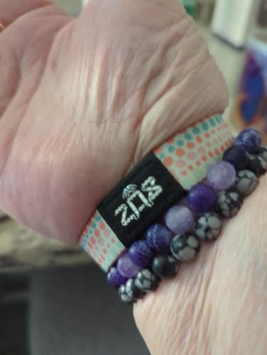 Close-up of a reviewer's wrist, wearing the colorful elastic Live By Faith bracelet stacked with purple and black beaded bracelets.