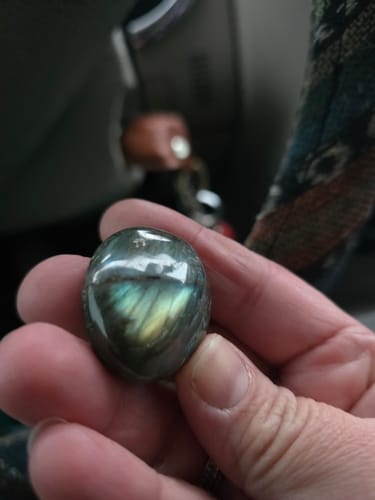 Close-up of a reviewer holding a polished, iridescent monthly crystal in their hand.