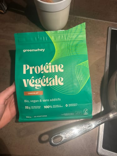 Un client tient le sachet vert de Protéine Végétale saveur chocolat dans une cuisine.
