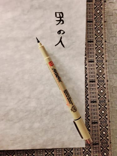 Customer's Sakura Pigma Brush Pen lying next to Japanese characters written on textured paper.
