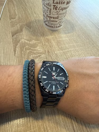 Cliente mostrando el reloj Seiko 5 negro metálico en su muñeca.