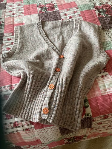 Reviewer's finished plain-knit vest from the Ladies Box kit, featuring a V-neck and bright orange buttons.