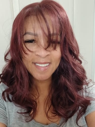 Reviewer showing her wavy Outre PEAK 715 wig styled with bangs in a cherry chocolate color.