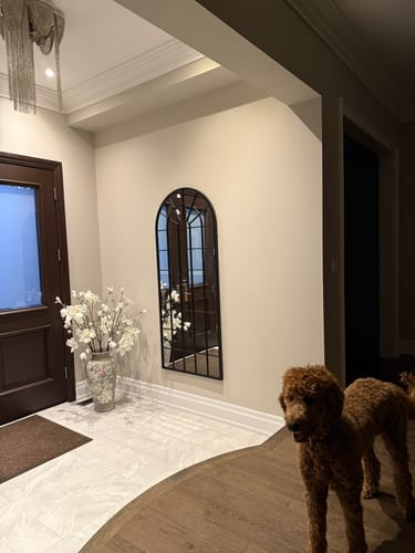Customer's black arched windowpane mirror mounted on a beige wall in a home entryway.