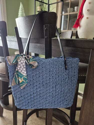 Customer's finished blue Aveline crochet Shoulder Bag hanging on a chair with a scarf tied to the strap.