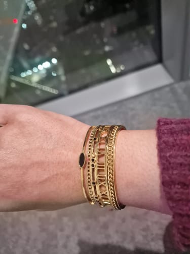 Reviewer wearing a stacked set of gold bangles, including the Oval Onyx Layered Bangle, on their wrist.