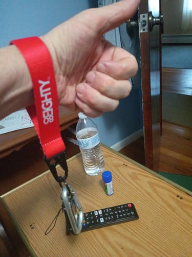 Reviewer gives a thumbs-up while wearing the red 80Eighty WristStrap around their wrist.