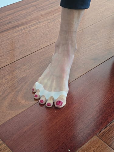 Customer's foot with a white Toe Separator being worn between the toes on a wood floor.