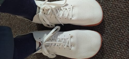 Asiakkaan jalassa olevat valkoiset Vaistoa Iloa Mid -tennarit tummien sukkien kanssa, ylhäältä kuvattuna.