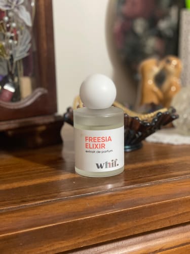 Customer's Freesia Elixir perfume bottle with a white cap, sitting on a wooden dresser.
