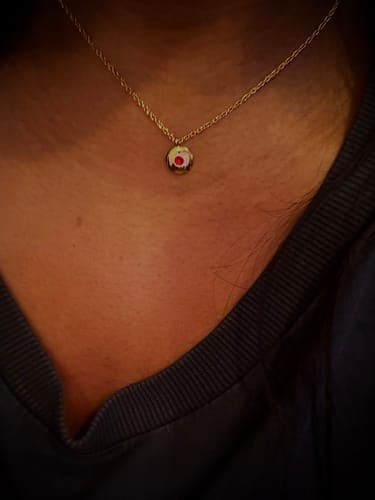 Close-up of a reviewer wearing the gold Birthstone Necklace with its round, red July birthstone.