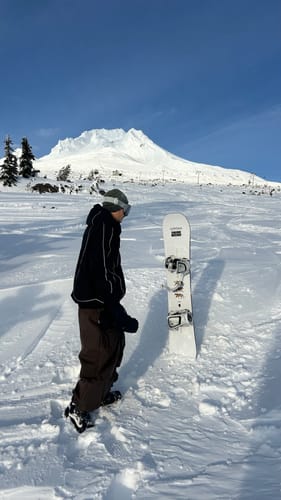 Customer wearing baggy dark brown snow pants on a snowy slope with a snowboard standing nearby.