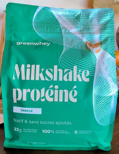 Un client montre le sachet vert de Milkshake protéiné à la vanille, posé sur une surface en bois.