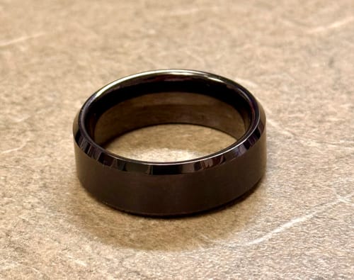 Reviewer's dark brushed ring with polished beveled edges resting on a stone surface.