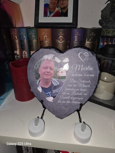 Kunde zeigt das personalisierte Schieferherz mit Foto und Gravur auf einem Ständer auf einem Regal.