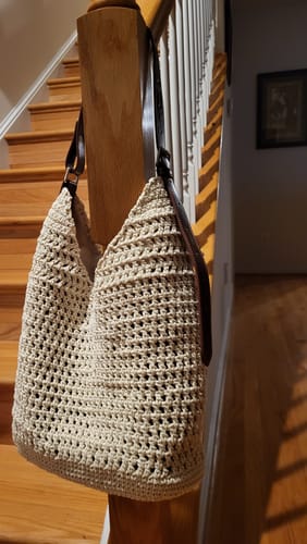 Customer's completed beige Haven Hobo bag from the crochet kit, hanging on a wooden stair rail.