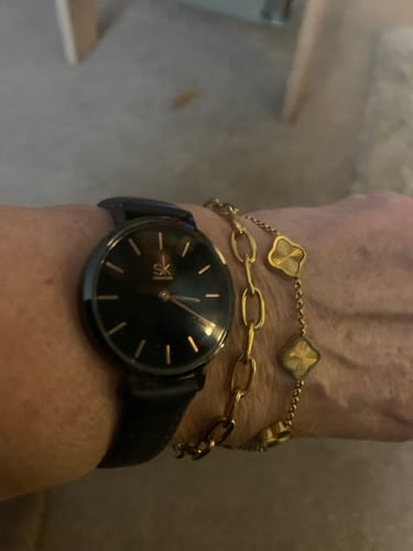 Customer's wrist showing two gold-colored bracelets from the December Bundle worn next to a black watch.