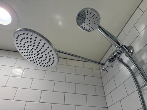 Reviewer's installed dual shower head with the rain and handheld heads angled apart in a white tiled shower.