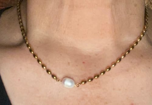 Close-up of a reviewer wearing a gold-tone necklace with a single pearl.