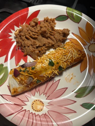 Reviewer's Chicken Enchilada with a light topping of cheese served with refried beans on a floral plate.