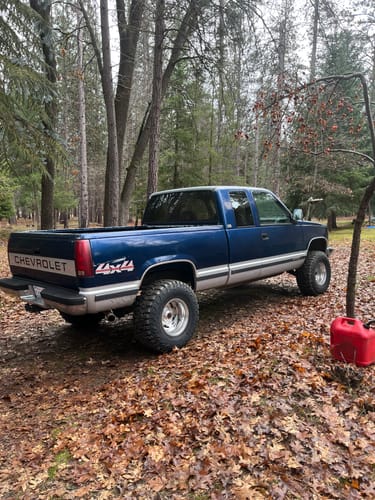 Customer's lifted blue Chevy K1500 truck parked in a wooded area after installing the upper control arms.