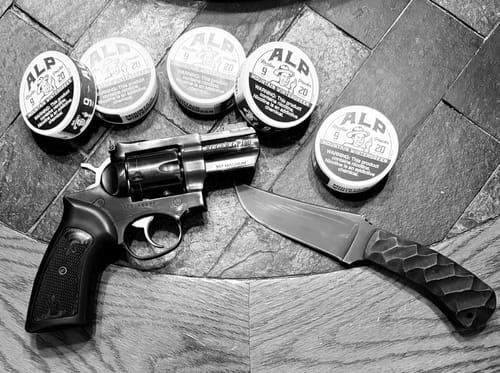 Customer's black and white photo of several Mountain Wintergreen Nicotine Pouches displayed with a revolver and a knife.