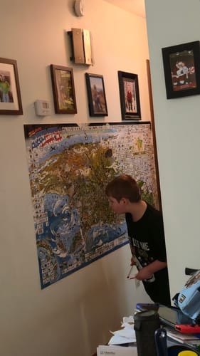 Reviewer's child closely examining the large World's Greatest Search & Discover poster on a hallway wall.