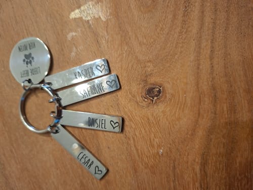 Recensent toont de 'Liefde Heeft Vier Poten' sleutelhanger met de namen Kasper, Safrane, Basiel en Cesar erop gegraveerd.