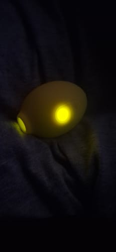 A reviewer's yellow Lem Clitoral Massager glowing from its button and opening in a dark setting.