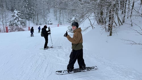 Reviewer gives a thumbs-up while snowboarding in the black baggy snow pants on a snowy slope.