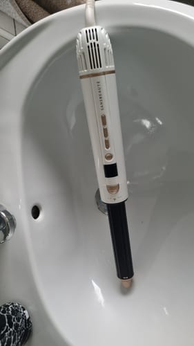 Recensent toont de witte SANSBEAUTÉ 8-in-1 airstyler met een zwart opzetstuk in een wastafel.