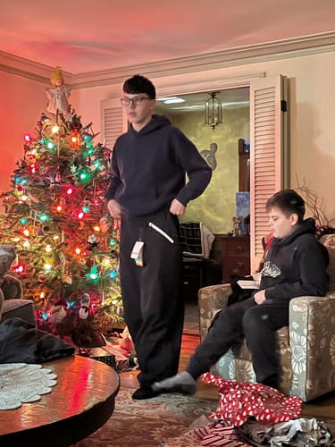 Customer trying on the baggy snow pants, showing the very oversized fit indoors next to a Christmas tree.