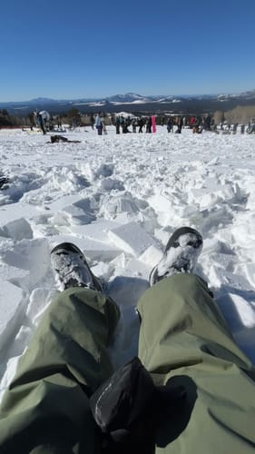 Customer's first-person view of their green baggy snow pants while sitting in the snow on a mountain.